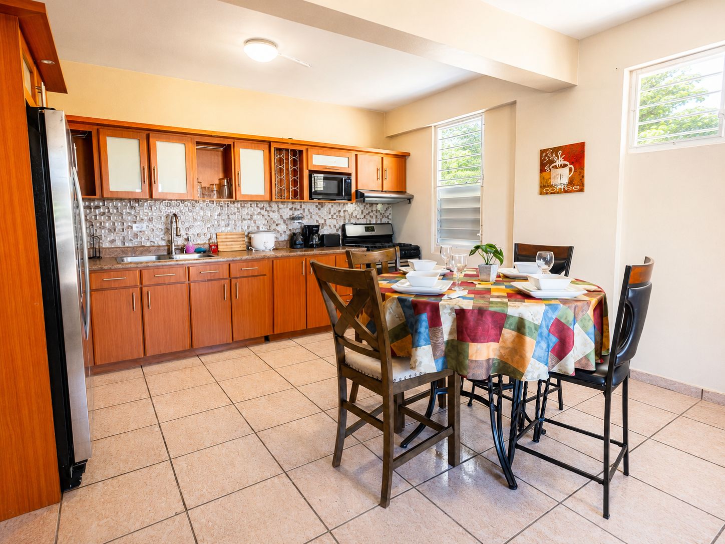 Una cocina con armarios de madera, salpicadero de azulejos y una mesa de comedor preparada para cuatro personas con sillas.