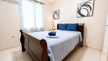 A bedroom with a bed, curtains, a bedside table, and two wall art pieces.