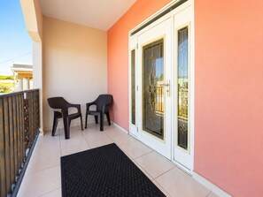 A balcony with two chairs and a black mat, a white door with glass panels, and a peach-colored wall. - Colinas del Atlantico for 18 People (Isabela)