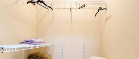 A small laundry room with a drying rack, shelves with folded towels, and an ironing board.