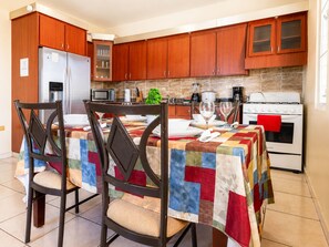 A kitchen with wooden cabinets, a refrigerator, a microwave, a stove, and a dining table with chairs. - Colinas del Atlantico for 18 People (Isabela)