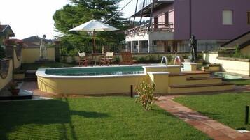 Un giardino sul retro con piscina, un patio con sedie e una statua.