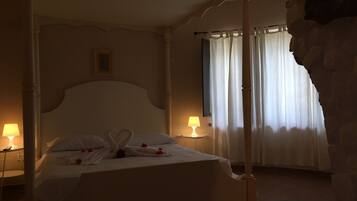 Un letto a baldacchino con un'accortoia a forma di cuore, un comodino con una lampada e un muro in pietra.