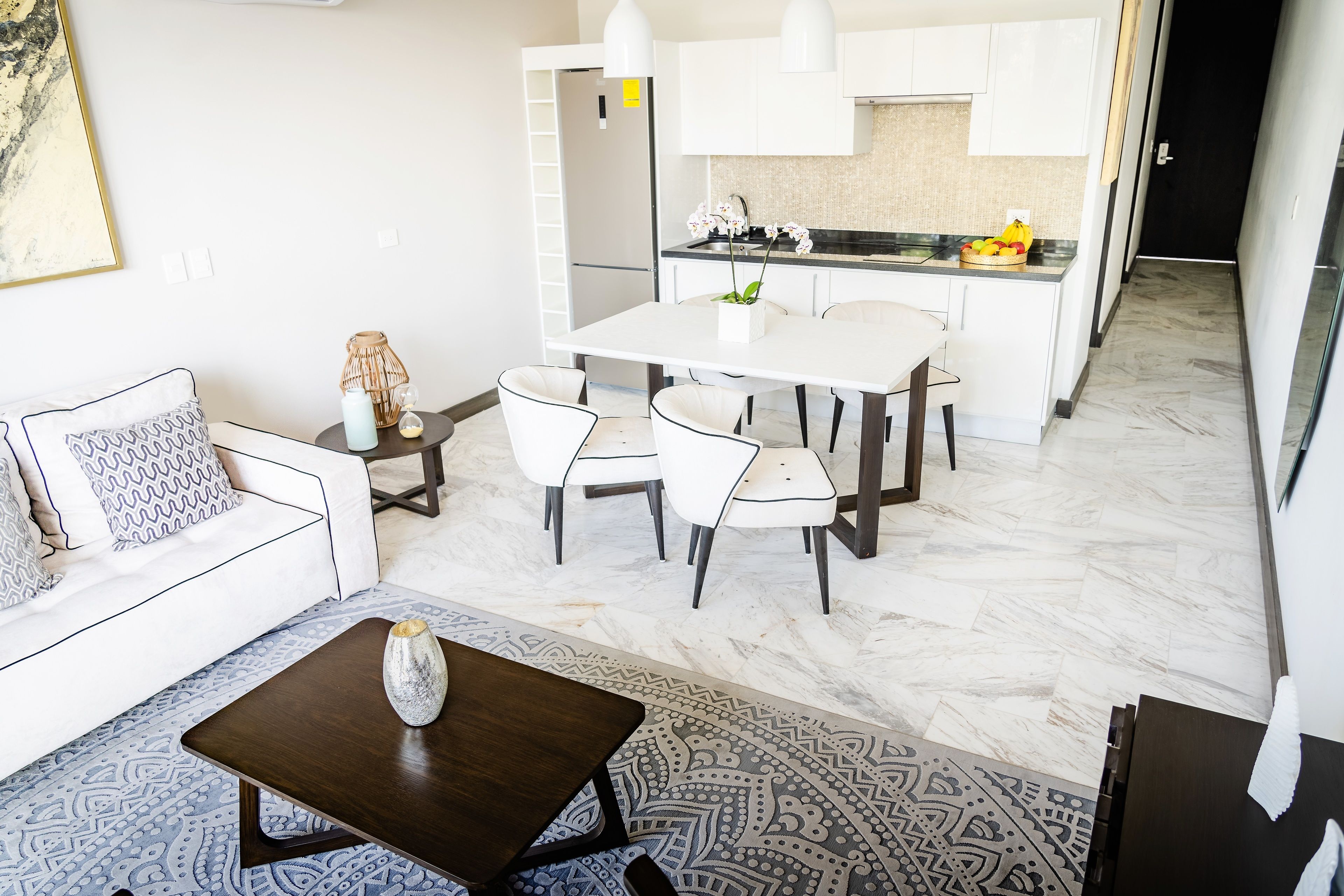 Un salon moderne avec un canapé blanc, une table basse et un coin repas comprenant une table et des chaises blanches.