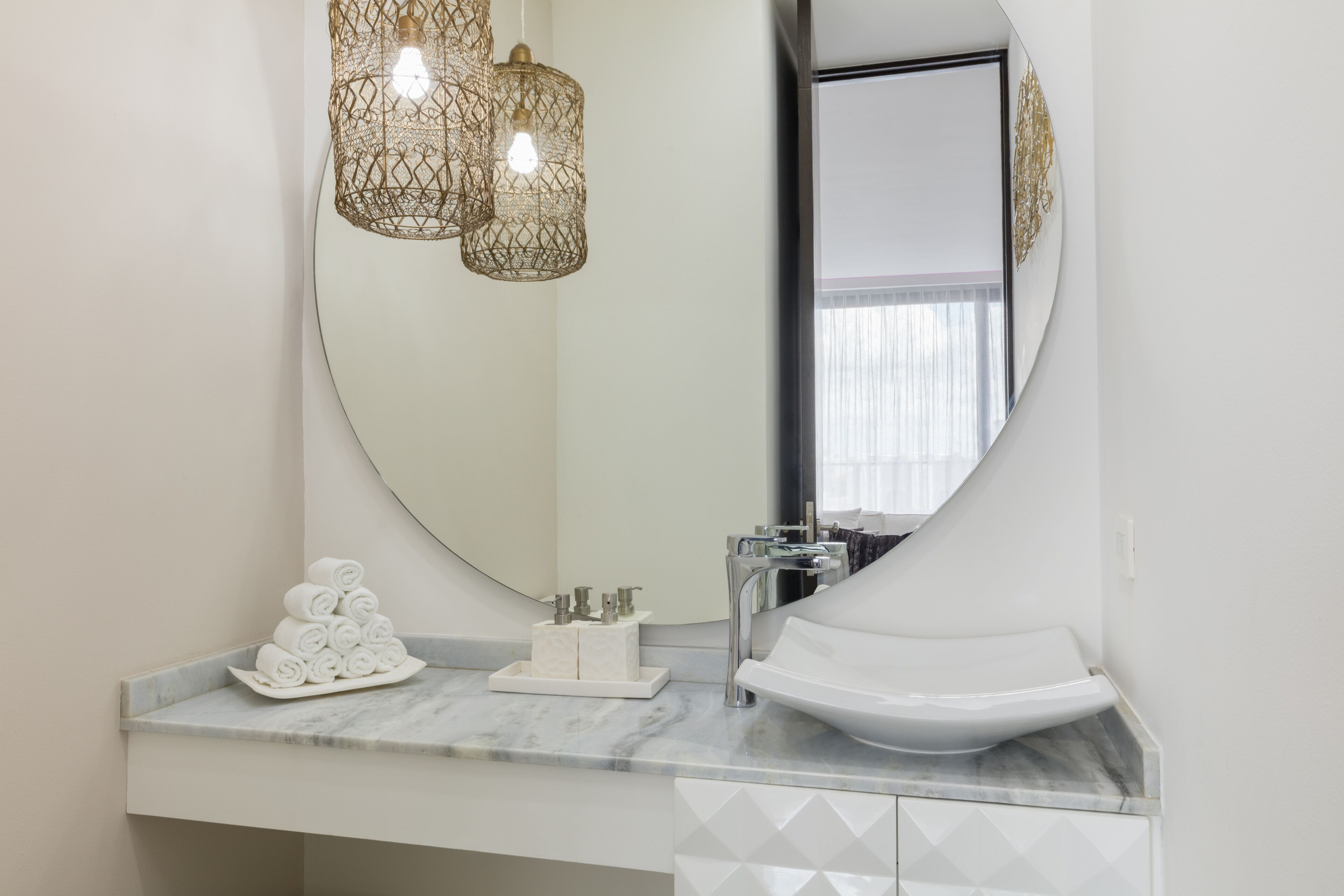 Un baño con un espejo redondo, un lavabo blanco y una encimera de mármol.