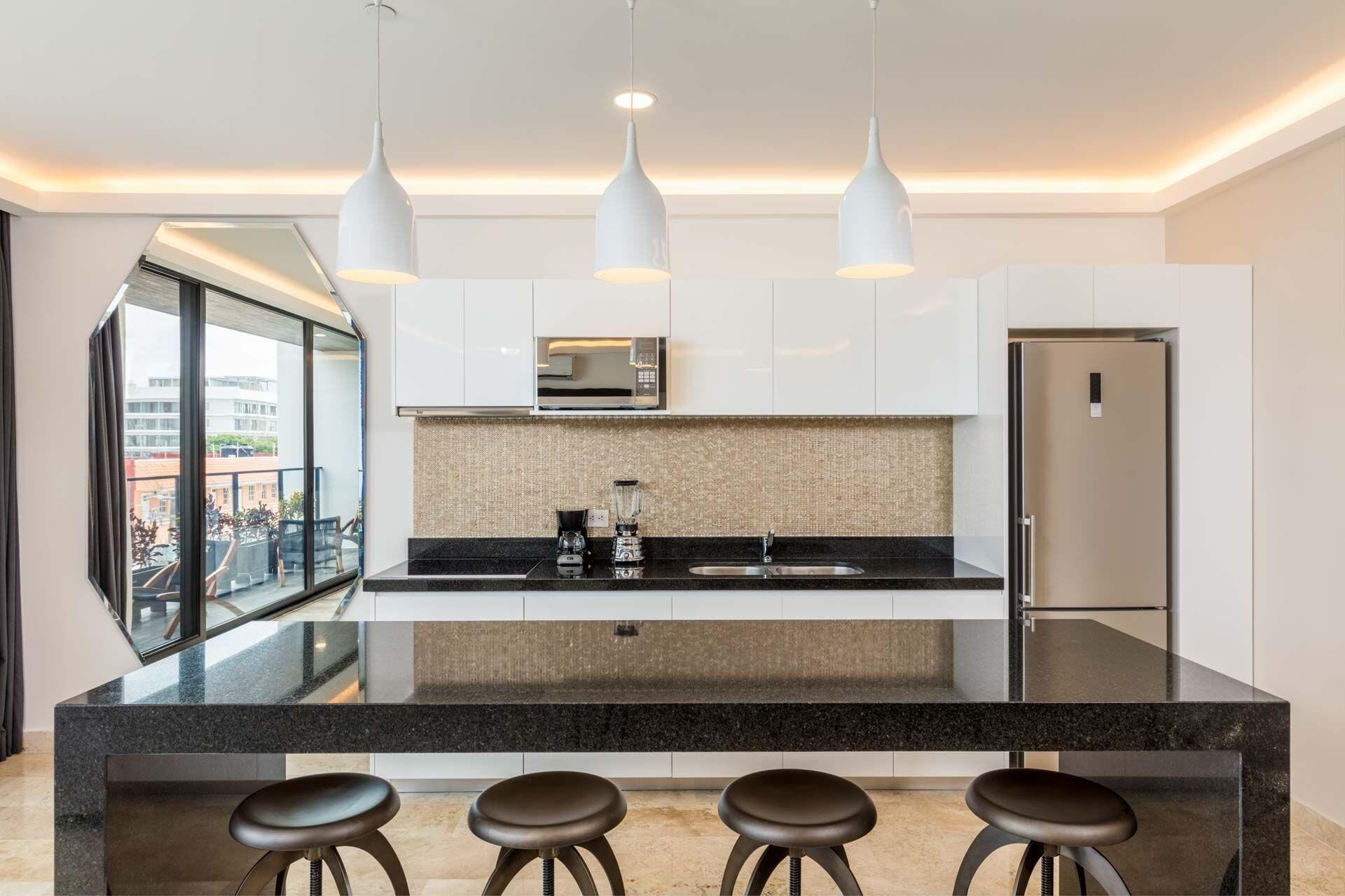 Una cocina moderna con una isla central, tres luces colgantes y un refrigerador de acero inoxidable.
