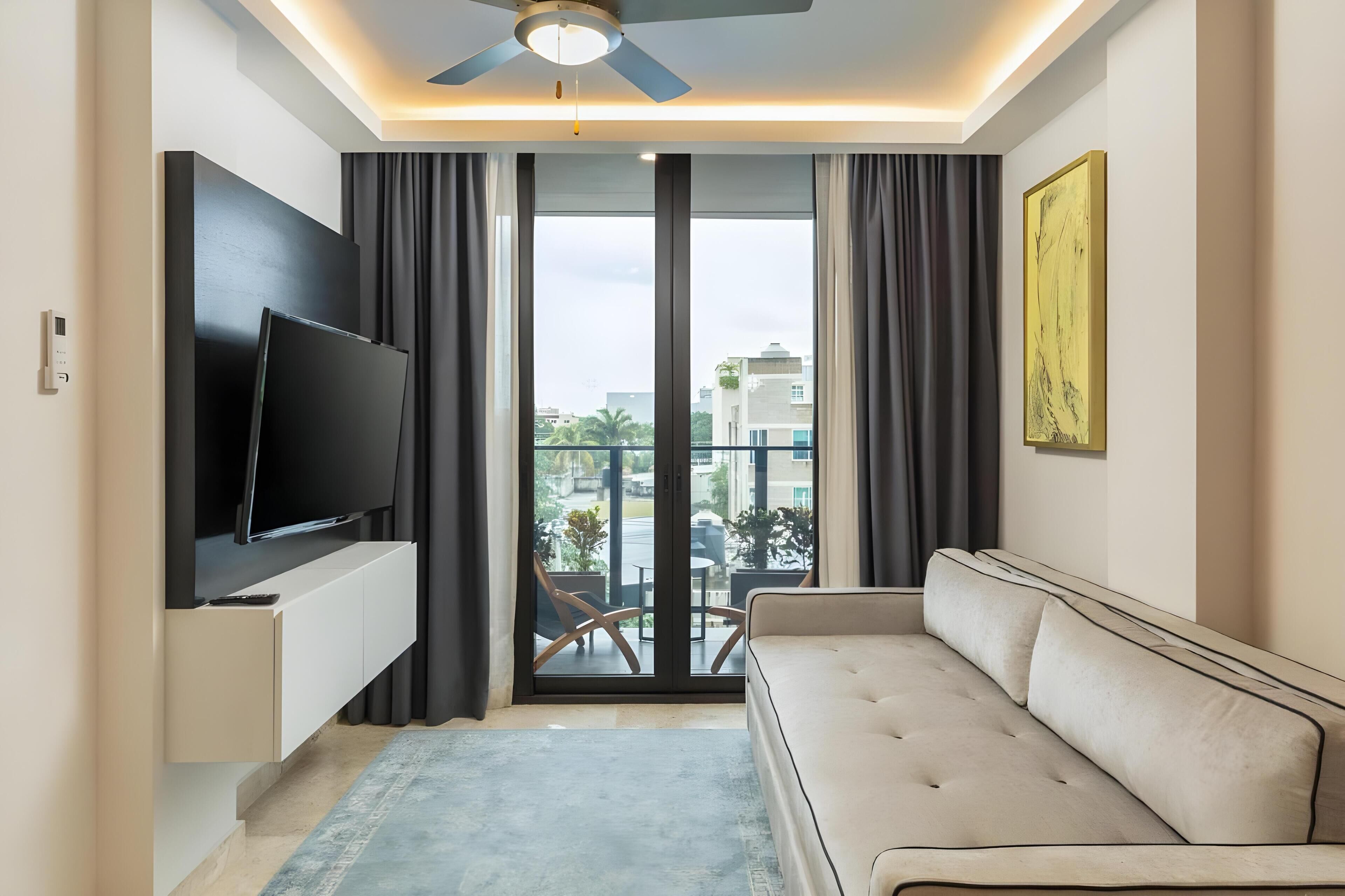 A modern living room with a flat-screen TV, a sofa, and a balcony with outdoor furniture.