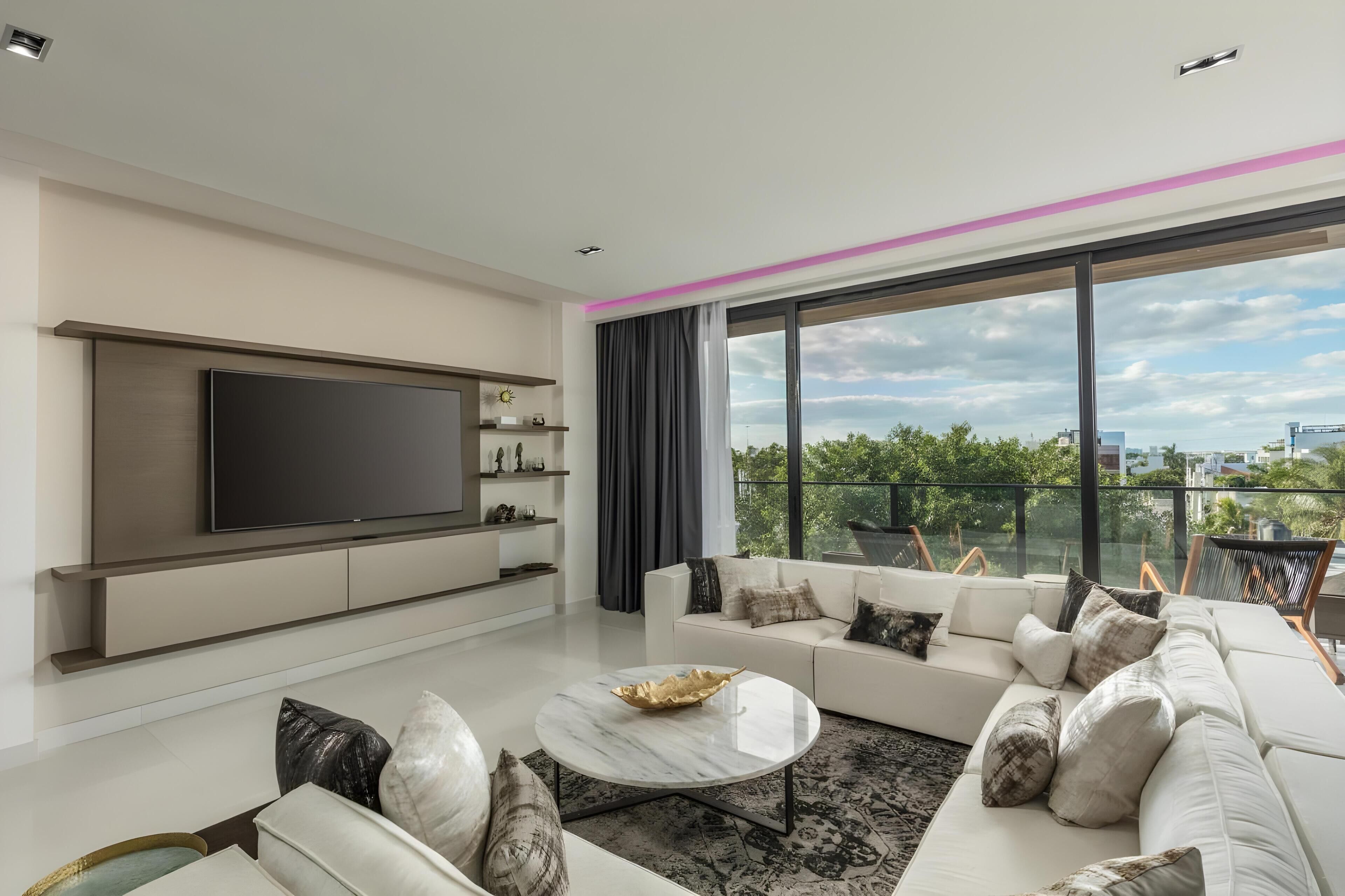 Una sala de estar moderna con un televisor de pantalla plana grande, un conjunto de sofá blanco y un balcón con vistas a la ciudad.