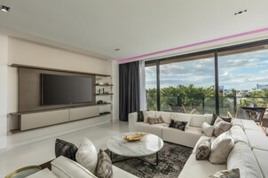 Una sala de estar moderna con un televisor de pantalla plana grande, un conjunto de sofá blanco y un balcón con vistas a la ciudad.