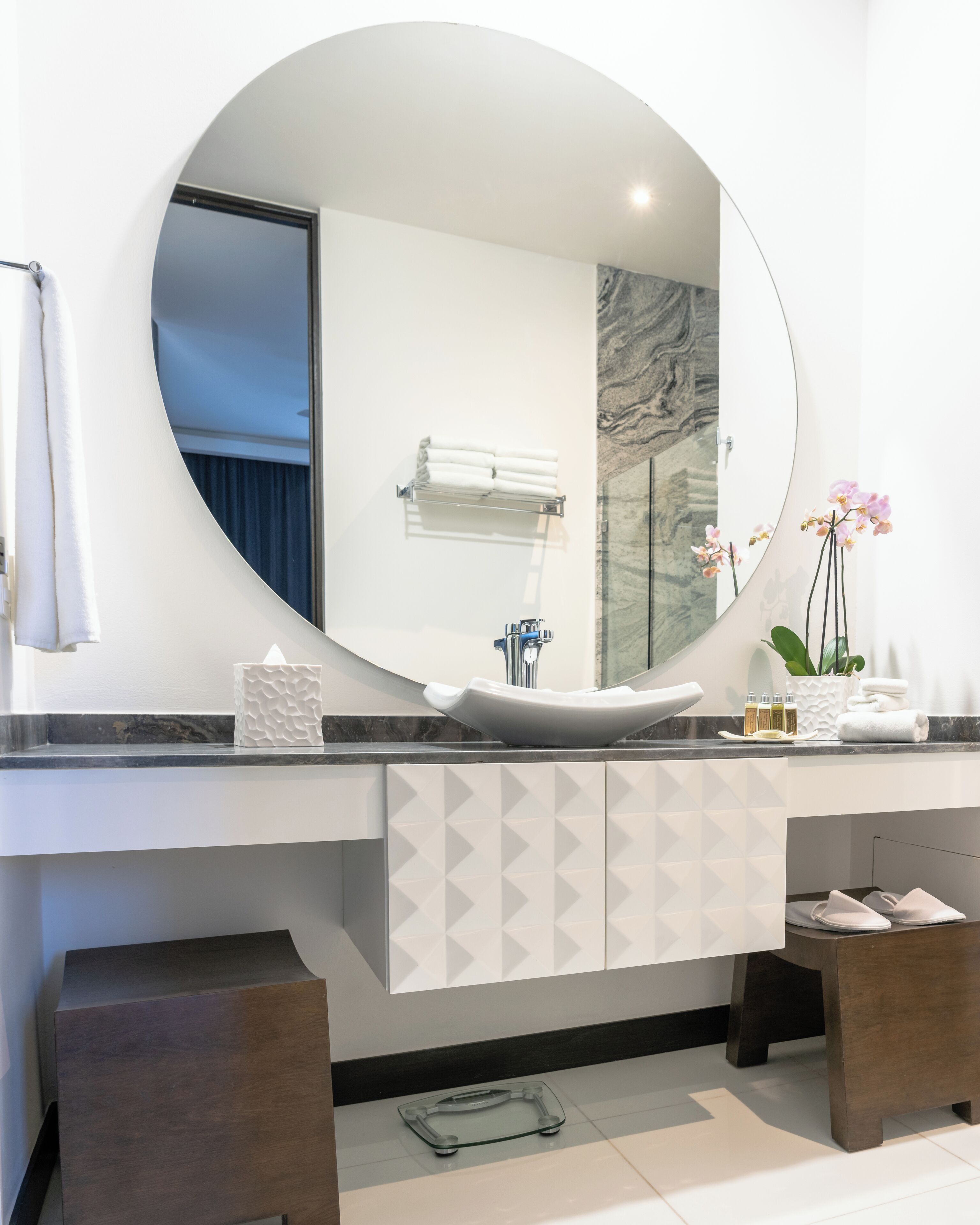 Ein modernes Badezimmer mit rundem Spiegel, weißem Waschbecken und Marmor-Spritzschutz.