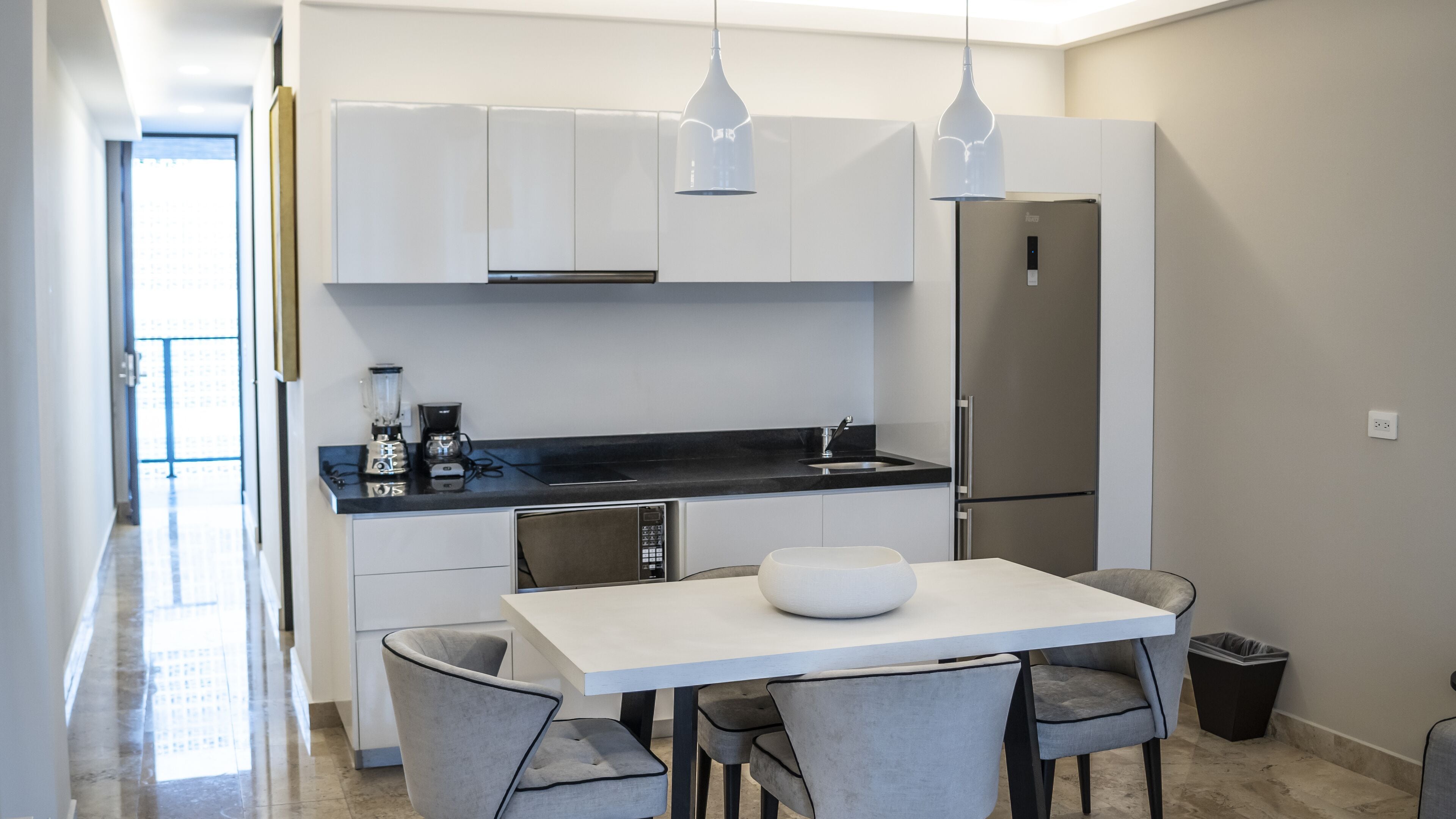 A modern kitchen with white cabinets, a black countertop, a built-in oven, a refrigerator, and a dining table with four chairs.