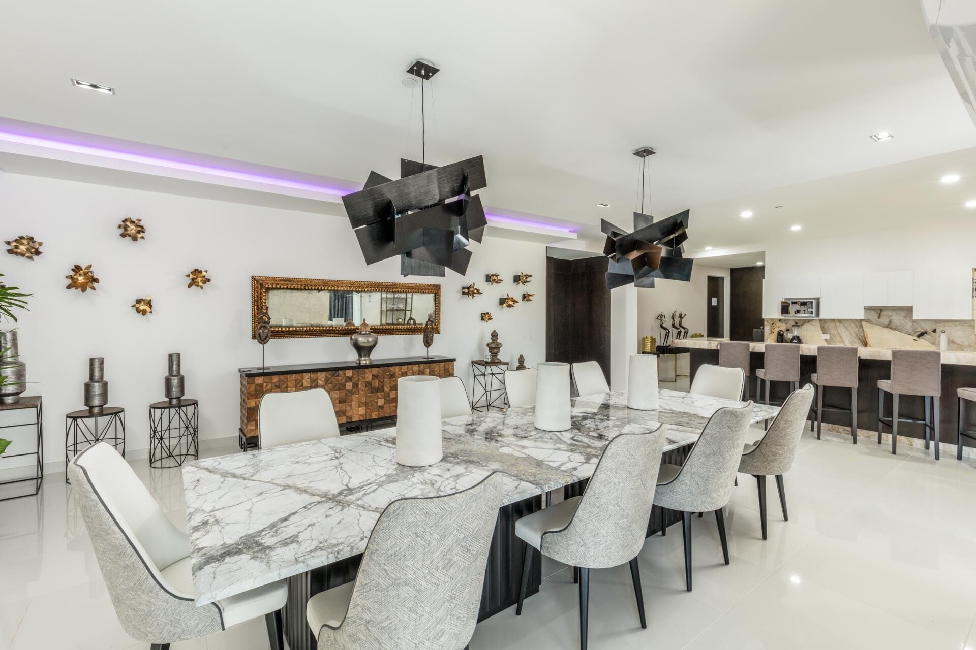 Un comedor moderno con una mesa de mármol, sillas blancas y una cocina al fondo.