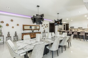A modern dining room with a marble table, white chairs, and a kitchen in the background.