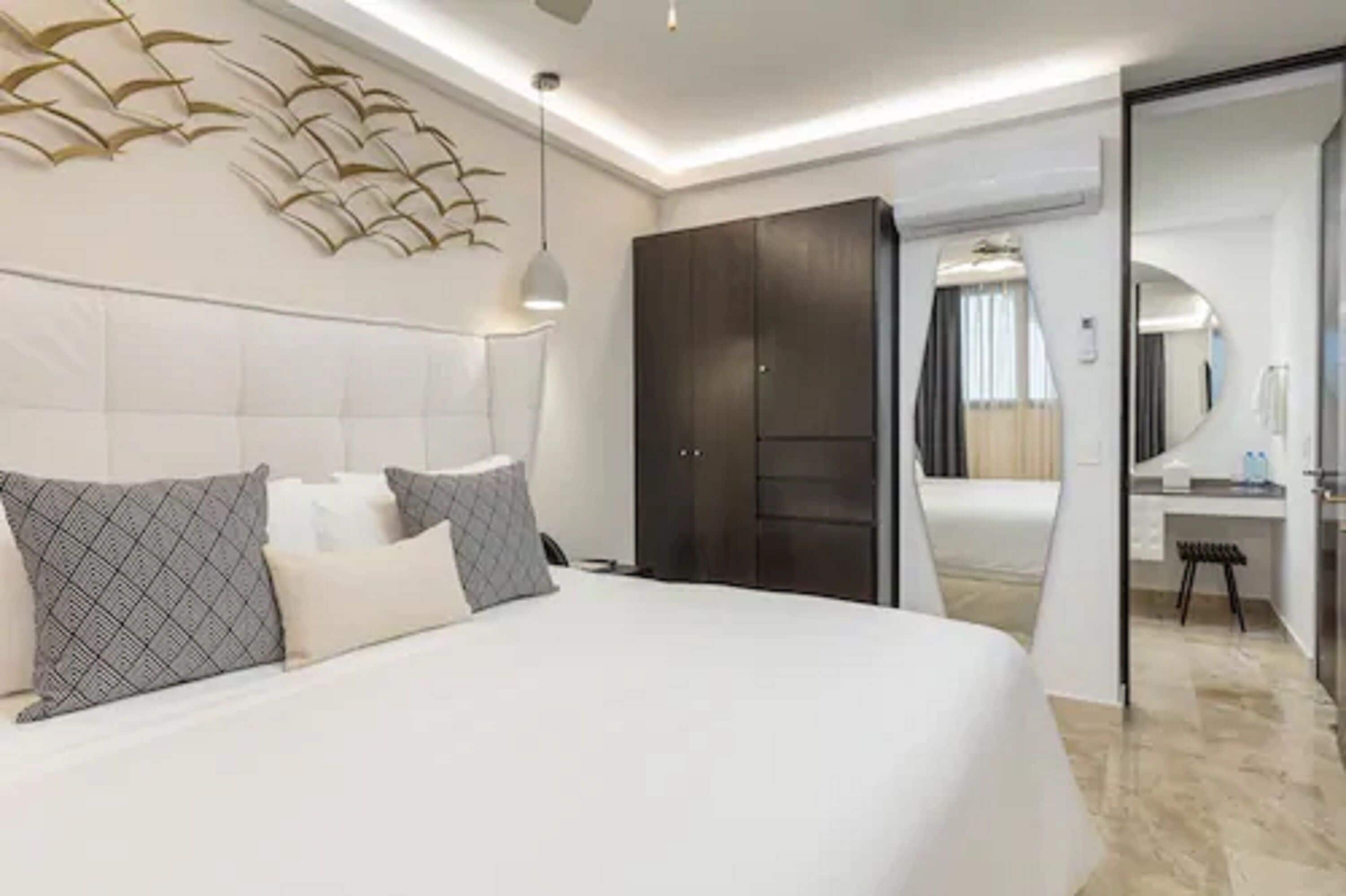Une chambre d’hôtel moderne avec un grand lit, une armoire sombre, un bureau et un miroir.