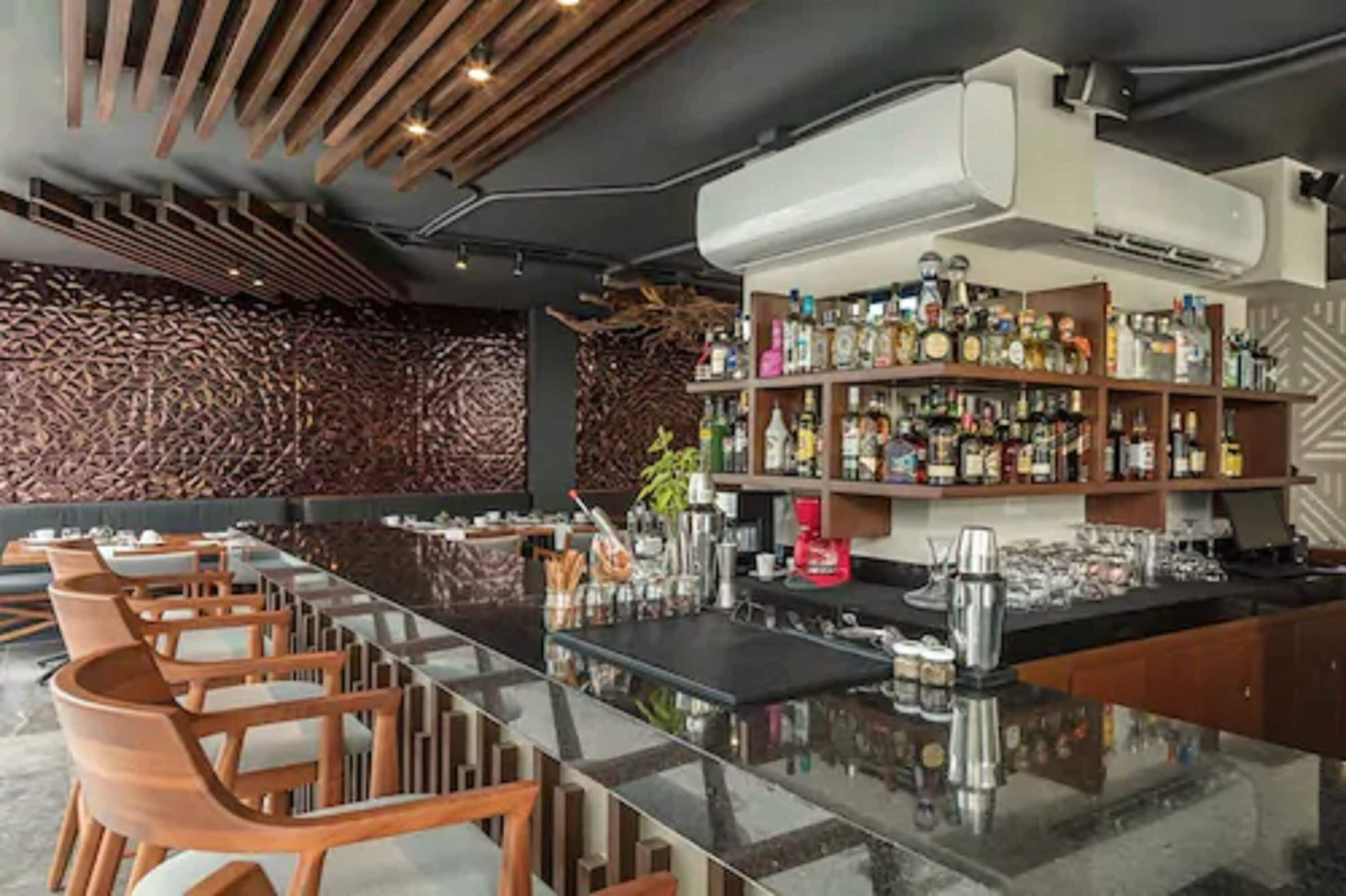 Een bar met een lange toonbank, houten stoelen en planken vol flessen.