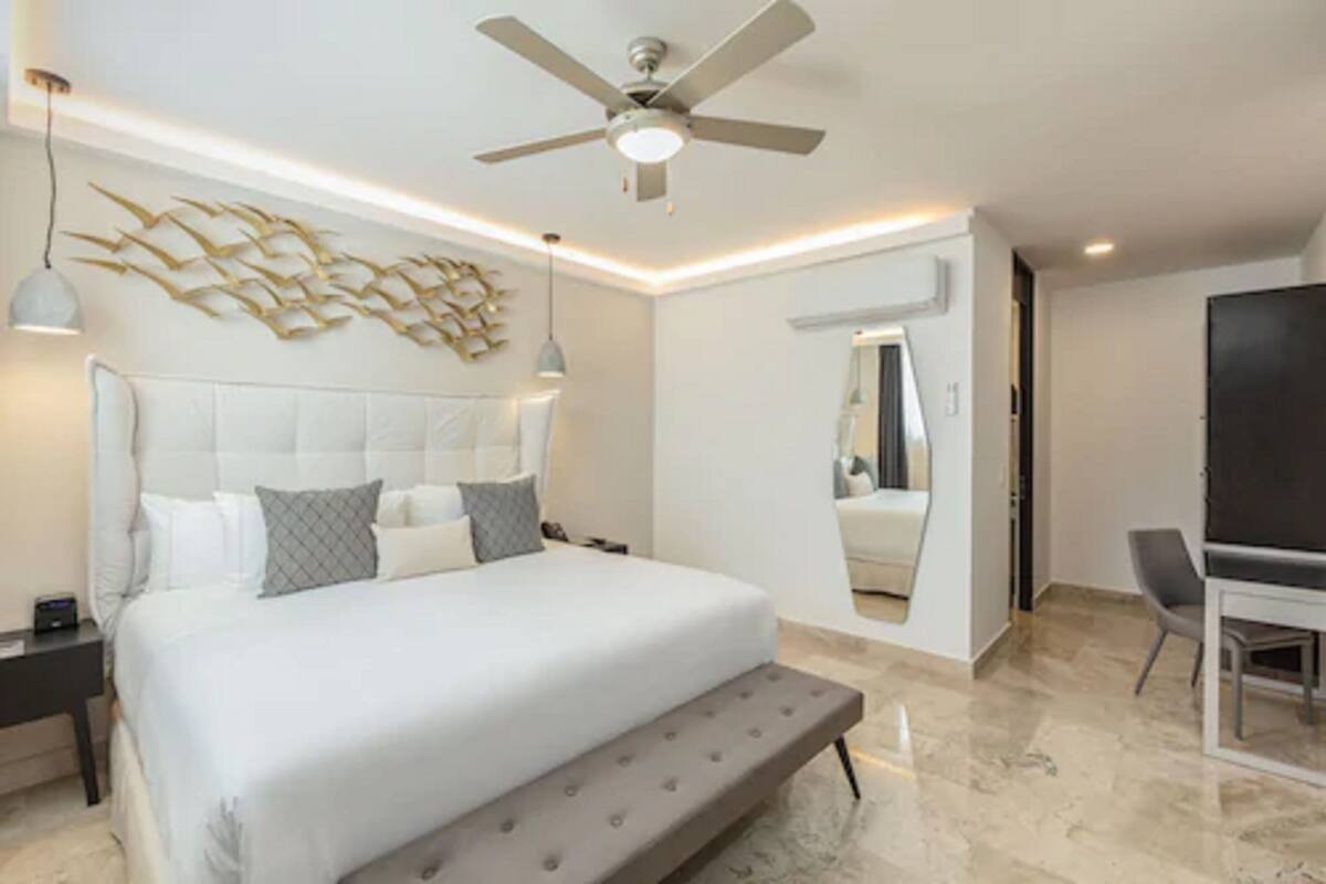 A modern bedroom with a large bed, a ceiling fan, and a wall-mounted mirror.