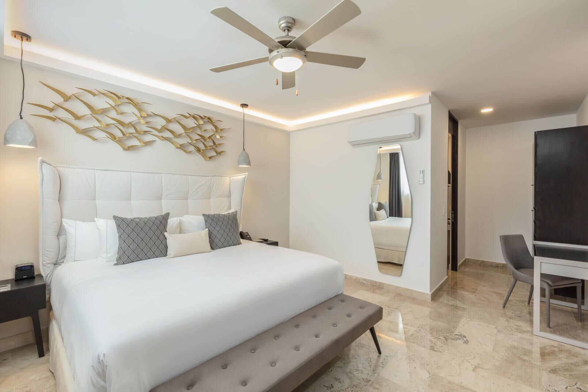 A modern bedroom with a large bed, a ceiling fan, a wall-mounted light fixture, and a mirror.