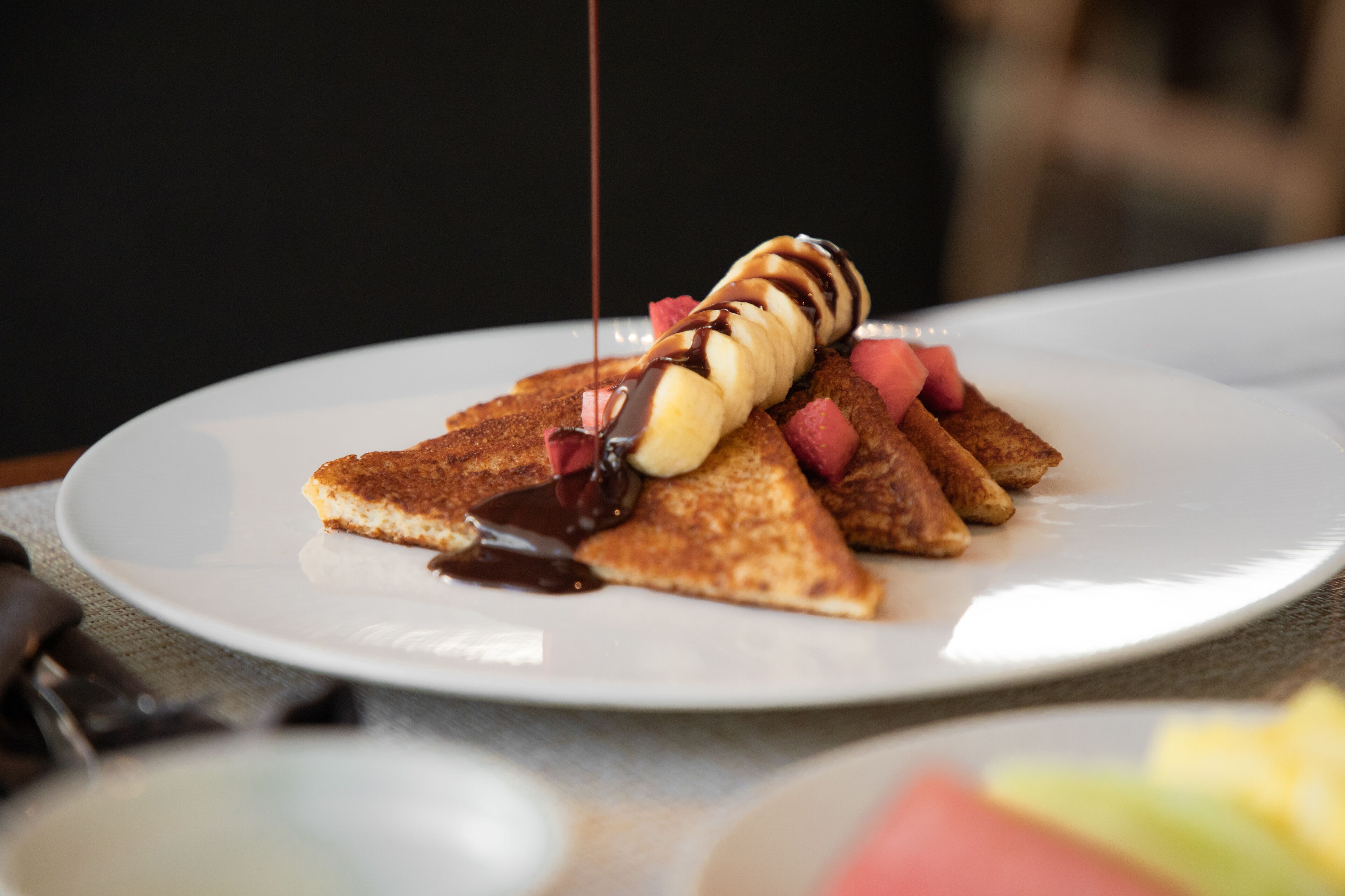 A plate with pancakes, bananas, and strawberries, topped with chocolate sauce.