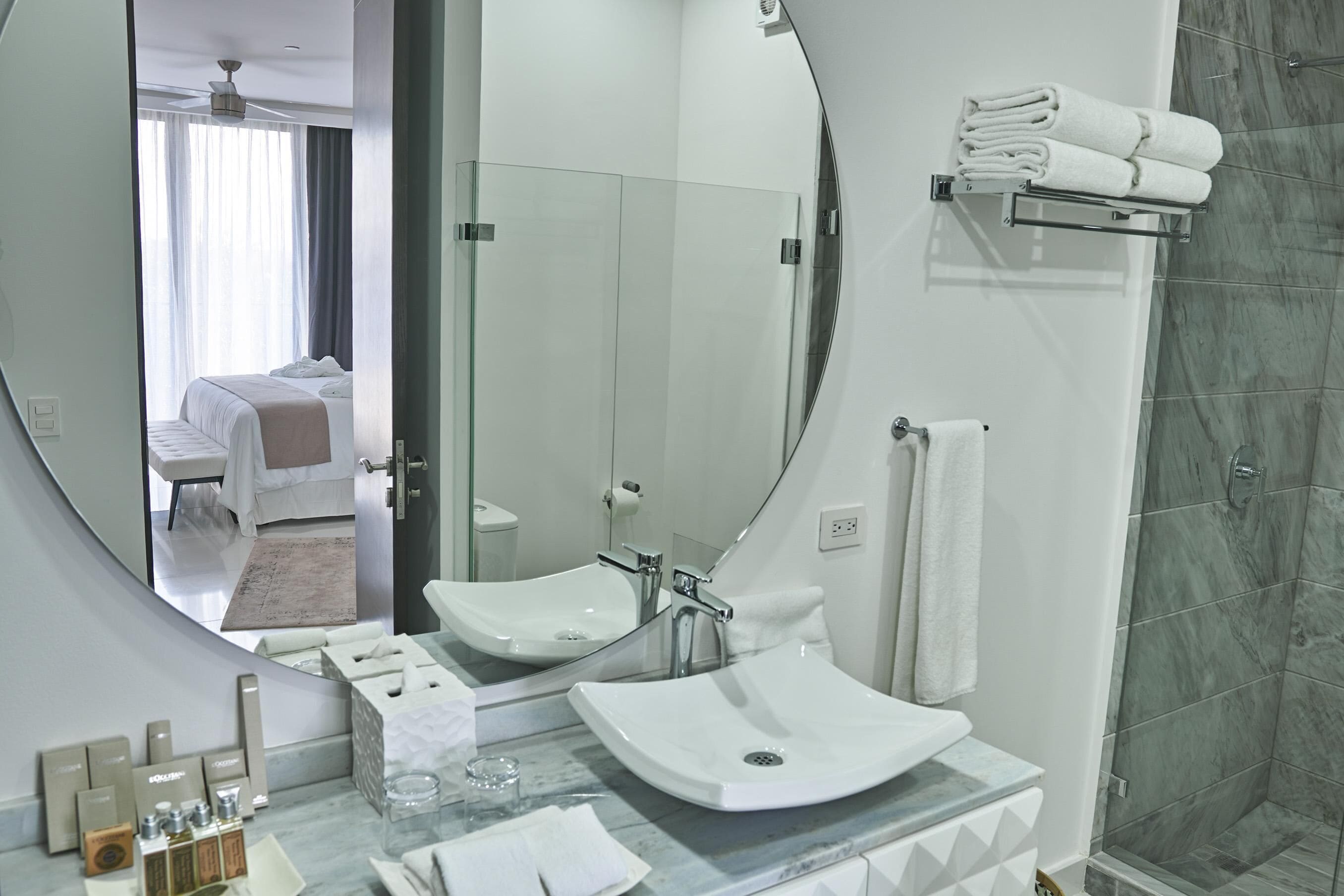 A modern bathroom with a large mirror, a white sink, a glass shower enclosure, and a towel rack.