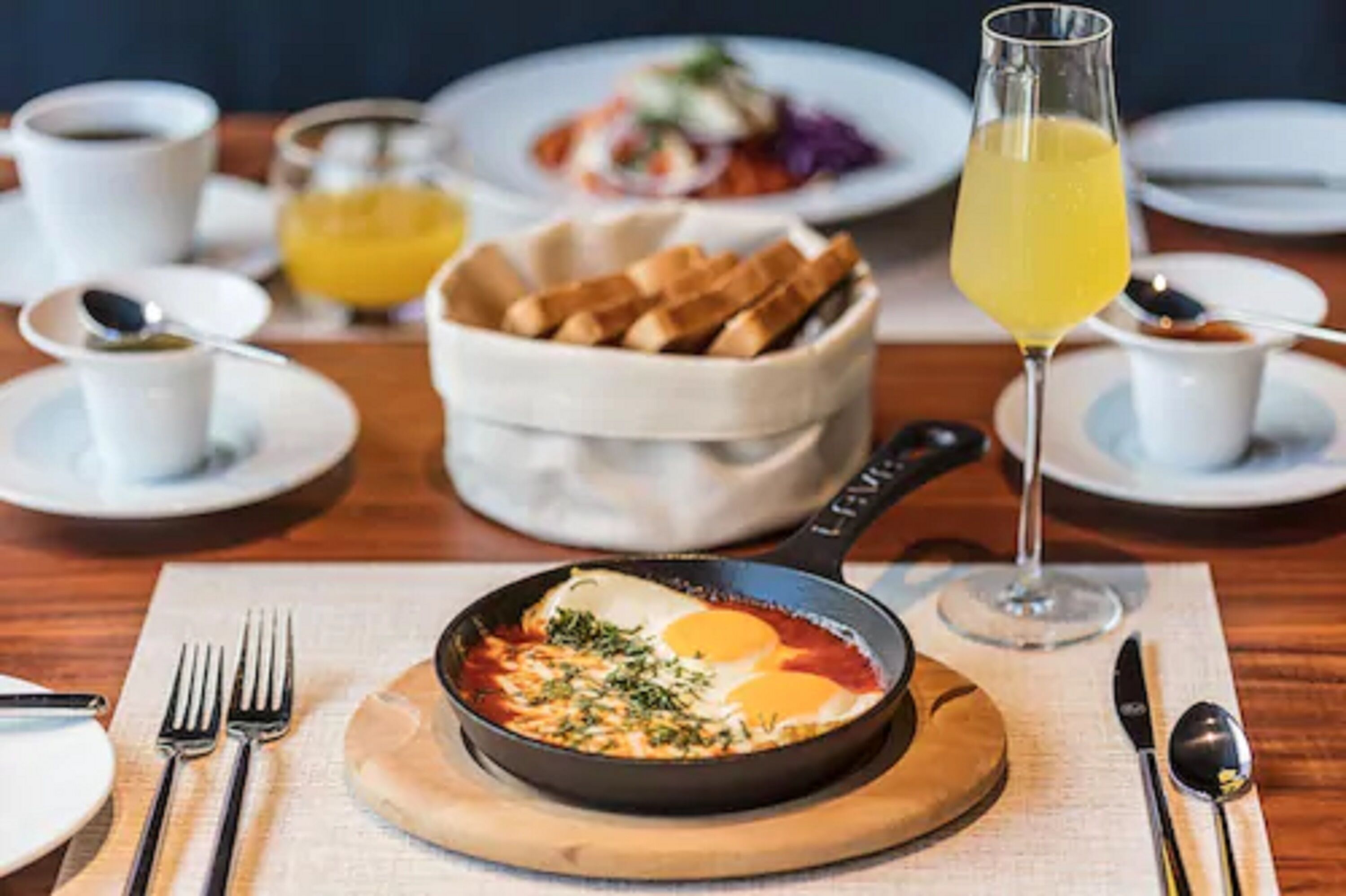 A breakfast setting with a skillet of eggs, toast, and a glass of orange juice.