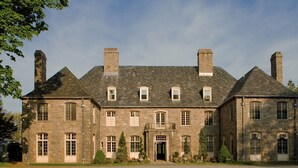 A large, historic stone building with multiple chimneys, a central entrance, and a symmetrical facade.