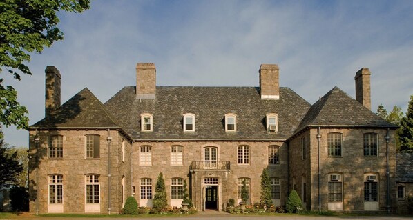 A large, historic stone building with multiple chimneys, a central entrance, and a symmetrical facade.