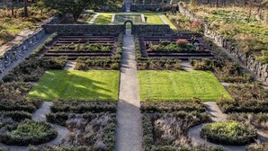 A formal garden with symmetrical pathways, neatly trimmed hedges, and a central water feature.
