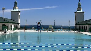 A swimming pool with lanes, a beach, and two towers in the background.