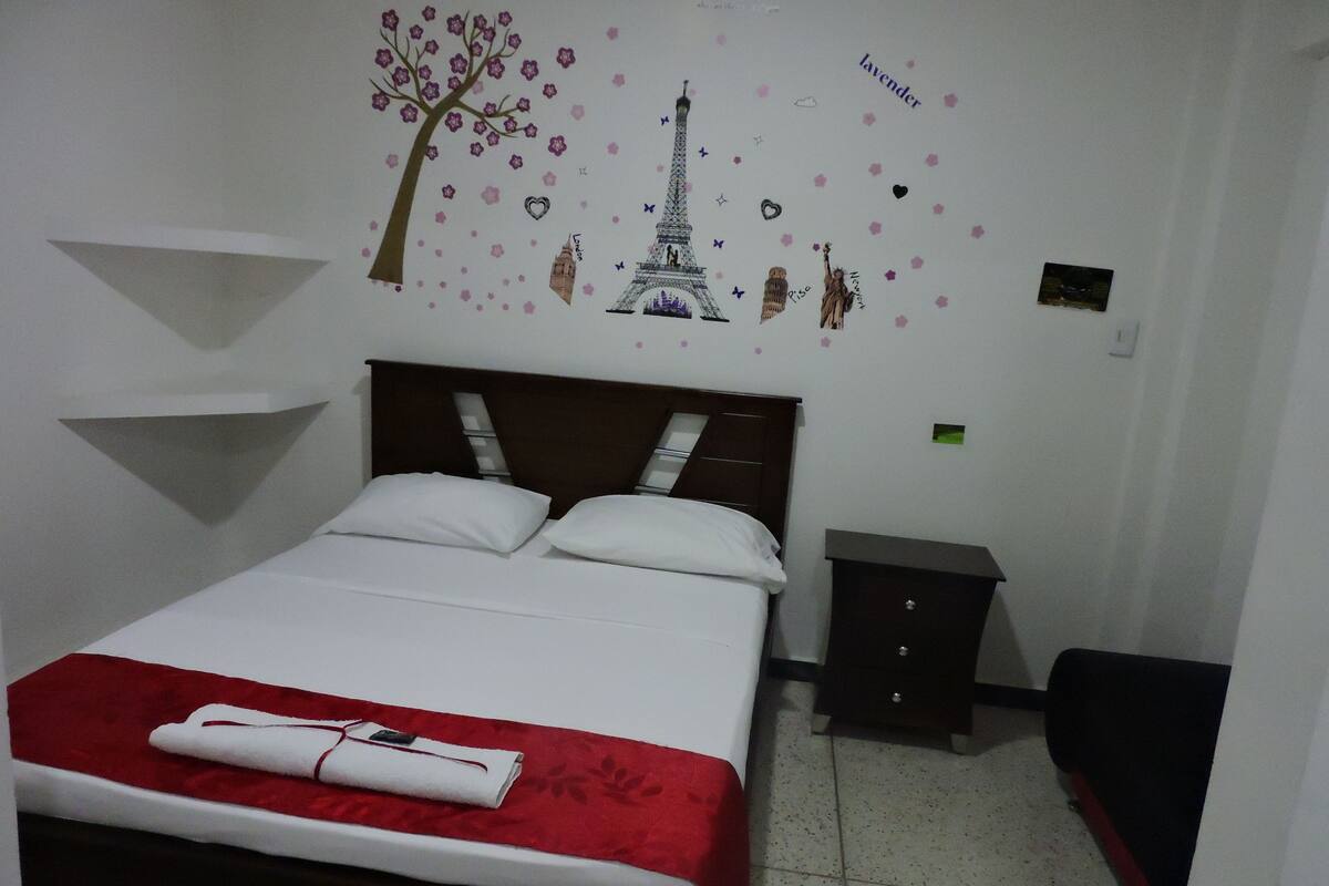 A neatly made bed with a red and white bedspread, a wooden headboard, and a small bedside table with a lamp.