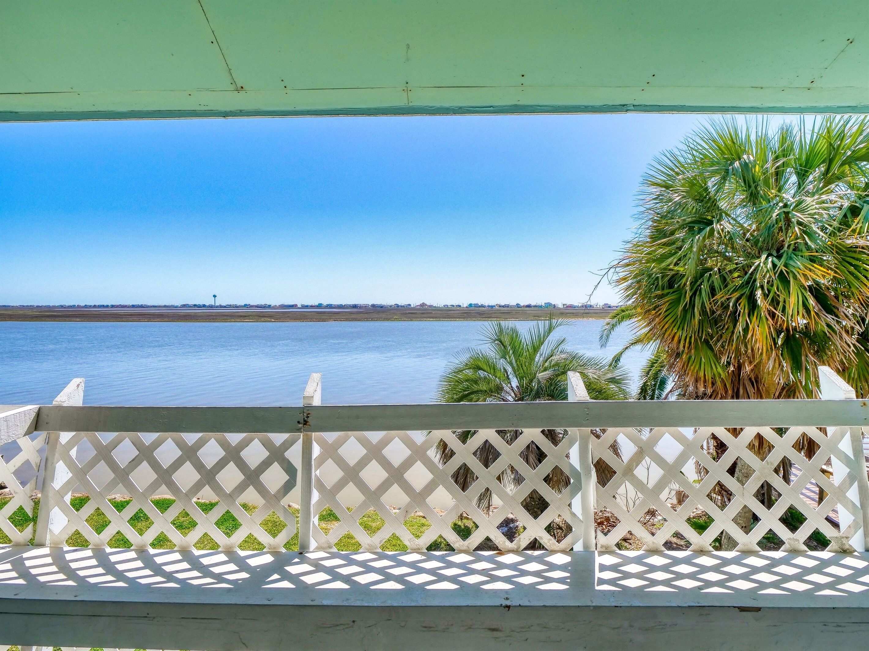 A view from a covered balcony overlooking a calm body of water with a distant shoreline and palm trees.