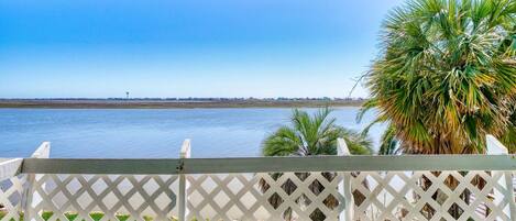 A view from a covered balcony overlooking a calm body of water with a distant shoreline and palm trees.