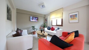Uma sala de estar com um sofá branco, um sofá vermelho, uma mesa de centro e uma televisão na parede.