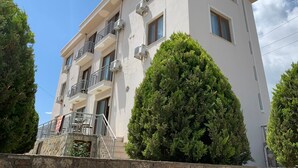 Um edifício de vários andares com varandas, aparelhos de ar condicionado e uma parede de pedra ao primeiro plano.