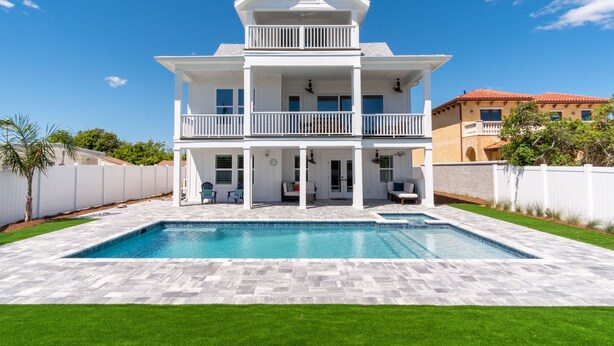 Ein zweistöckiges Haus mit Swimmingpool, überdachter Terrasse und weißem Zaun.