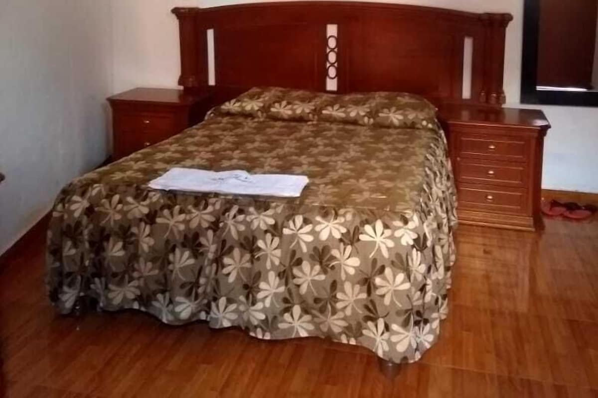 A bedroom with a wooden bed, a nightstand, a dresser, and a framed picture on the wall.