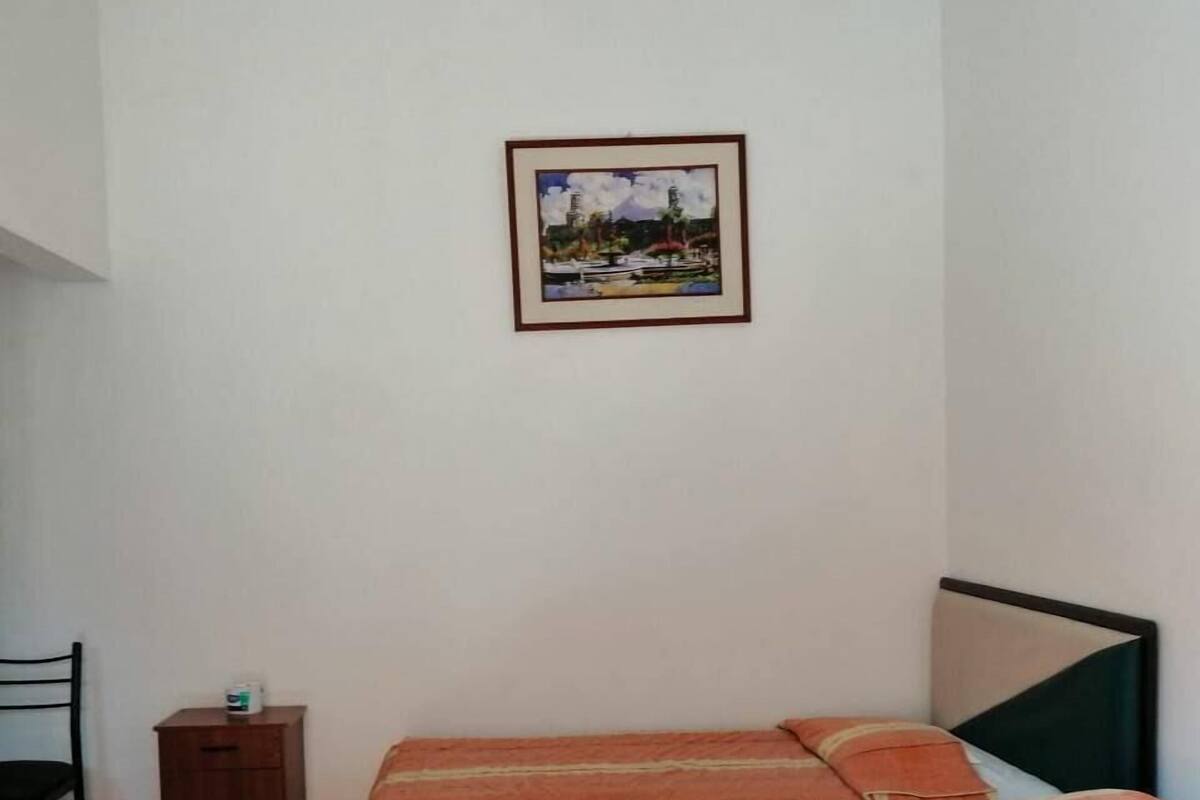 Ein Schlafzimmer mit einem Bett, einem Nachttisch, einem Sessel und einem gerahmten Bild an der Wand.