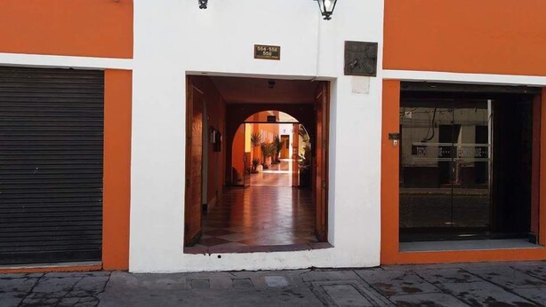 A building entrance with a closed shutter on the left, an open archway leading to a corridor, and a visible sign above the archway. - Hostal Characato Suite (Arequipa)