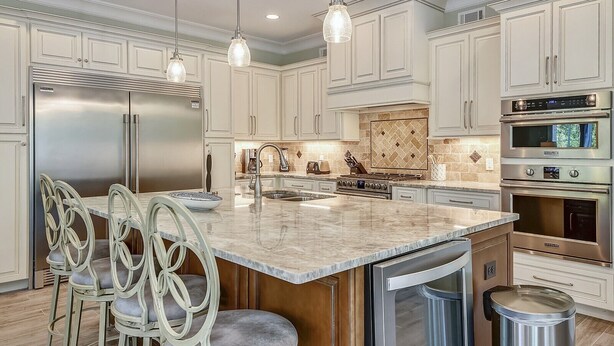Una cocina moderna con armarios blancos, electrodomésticos de acero inoxidable e isla de mármol con taburetes de bar.