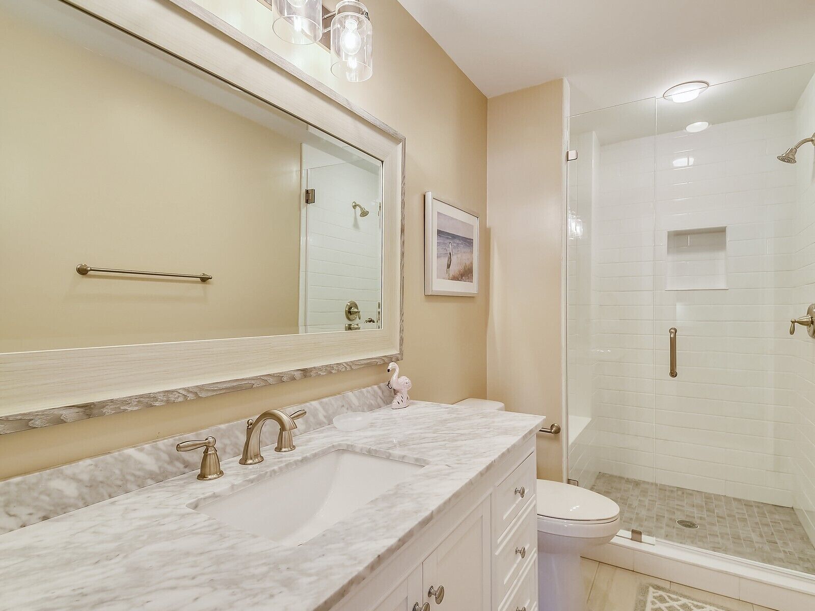 A bathroom with a large mirror, two sinks, a toilet, and a glass-enclosed shower.