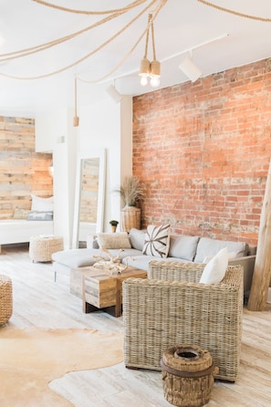 Un salon chaleureux avec un mur en briques, des meubles en osier et un plancher en bois.