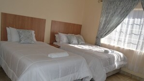 A hotel room with two beds, each with a wooden headboard, white bedding, and a window with sheer curtains.