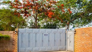 A gated entrance with a number plate, a brick wall, and a tree with red flowers.