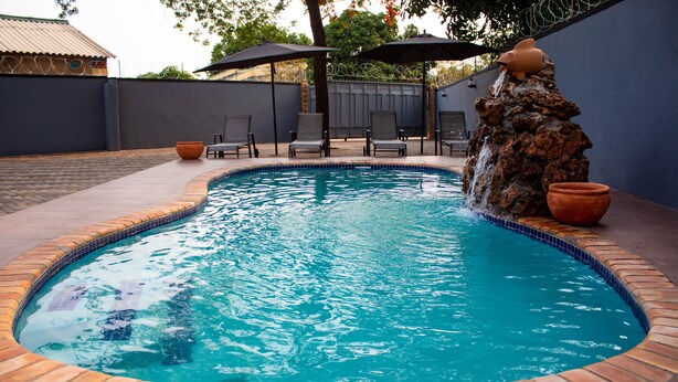 A swimming pool with a tiled edge, surrounded by a brick border. There are lounge chairs and umbrellas in the background.