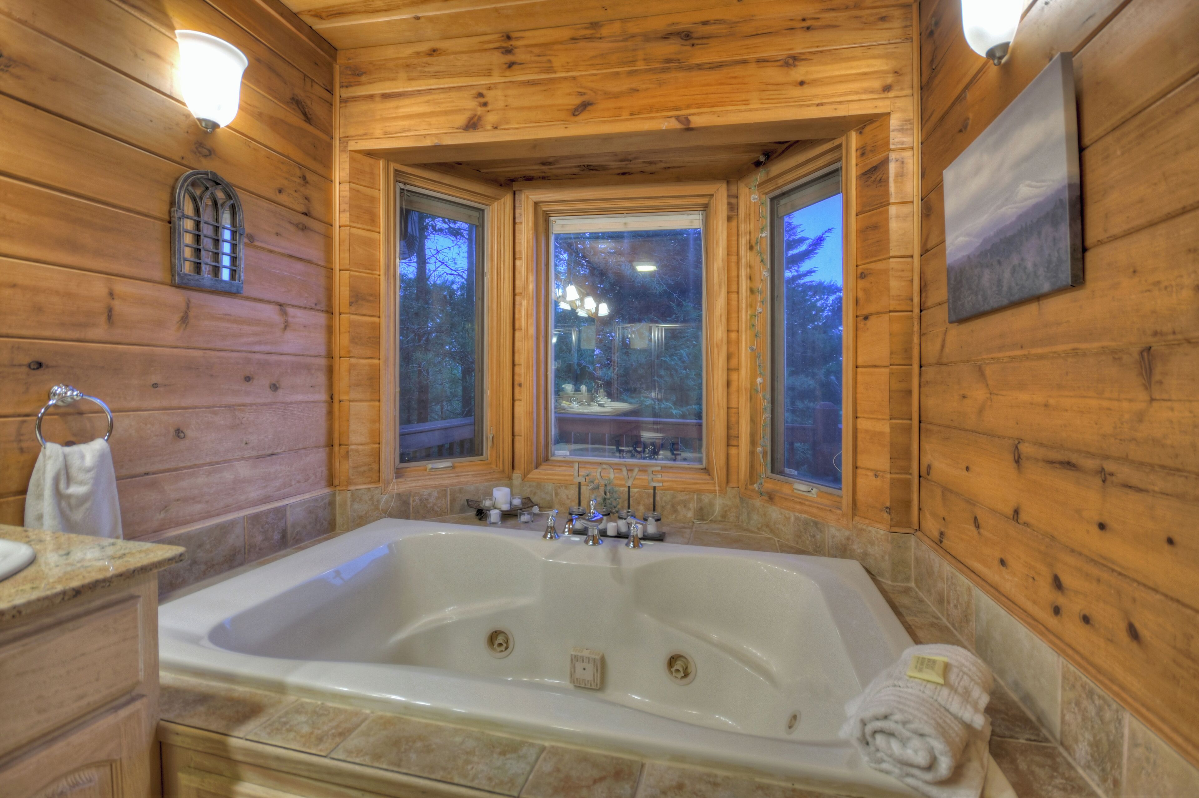 A wooden cabin bathroom with a large bathtub, a window, and a wooden wall with a picture.