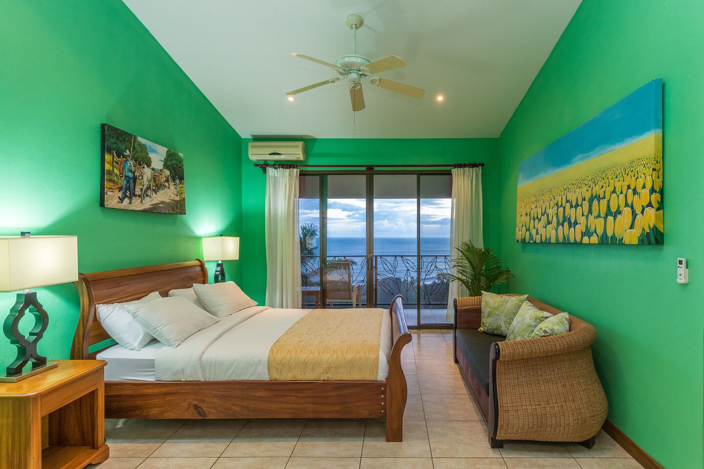 A hotel room with a bed, a chair, a balcony with a view, and a painting on the wall.
