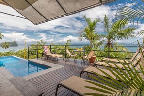 A pool area with lounge chairs and a table, surrounded by tropical plants and overlooking a body of water. - Vista Oceana, Stunning Ocean View Villa (Quepos)