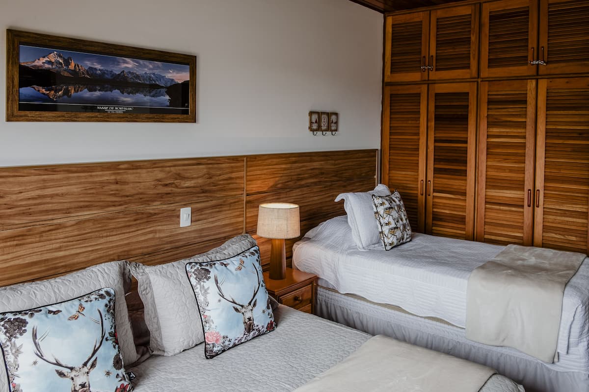 Habitación de hotel con dos camas, cabecero de madera, televisor montado y mesita de noche con lámpara.