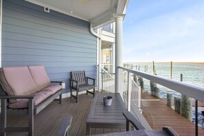 Eine Holzterrasse mit einer Sitzecke, einem Tisch und einem Geländer mit Blick auf ein Gewässer.