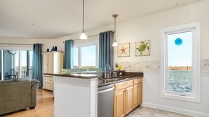 Una cocina moderna con una isla central, armarios de madera y vistas al mar a través de un amplio ventanal.