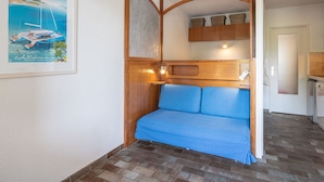 Quarto compacto com um sofá azul estampado com bolinhas, cabeceira de madeira e um quadro de barco na parede.